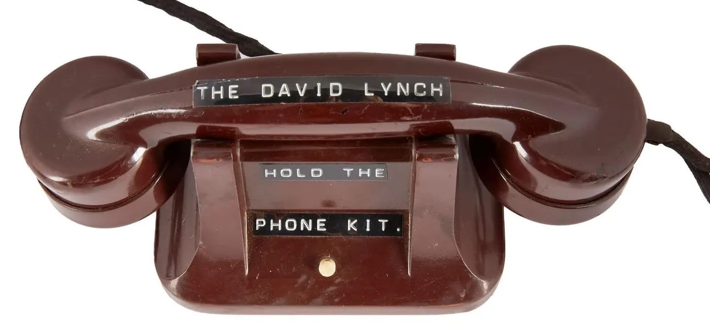 a maroon vintage phone with wording stuck to it that reads, "THE DAVID LYNCH HOLD THE PHONE KIT"