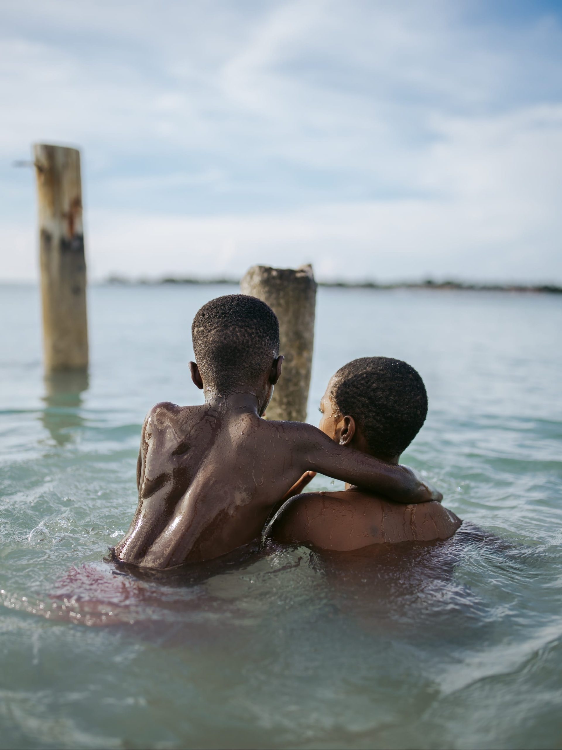 a photograph of two young Black boys swimming near an old pier
