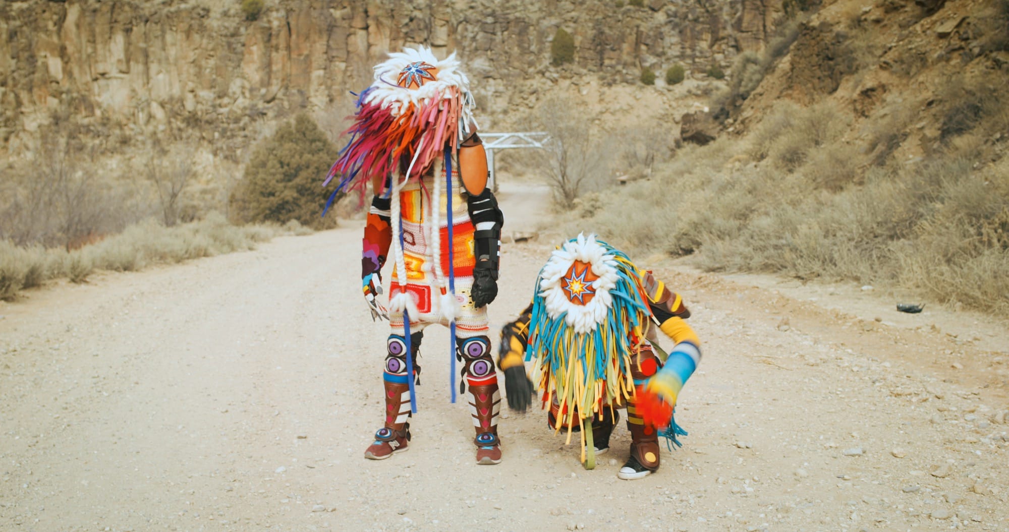 two Indigenous performers in the desert, wearing futuristic Native American garments